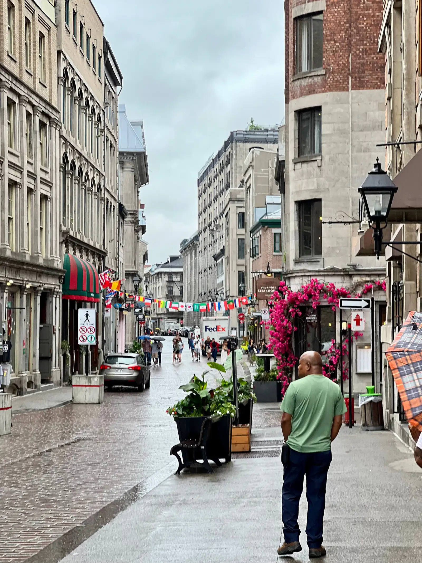 A narrow street in Old Montreal with flags, flowers and stone buildings
