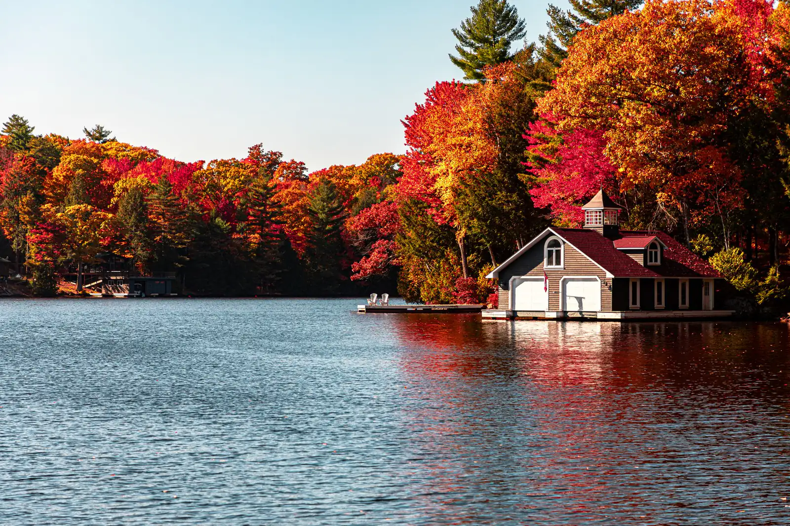 A boathouse on an Ontario lake surrounded by red and orange autumn forest