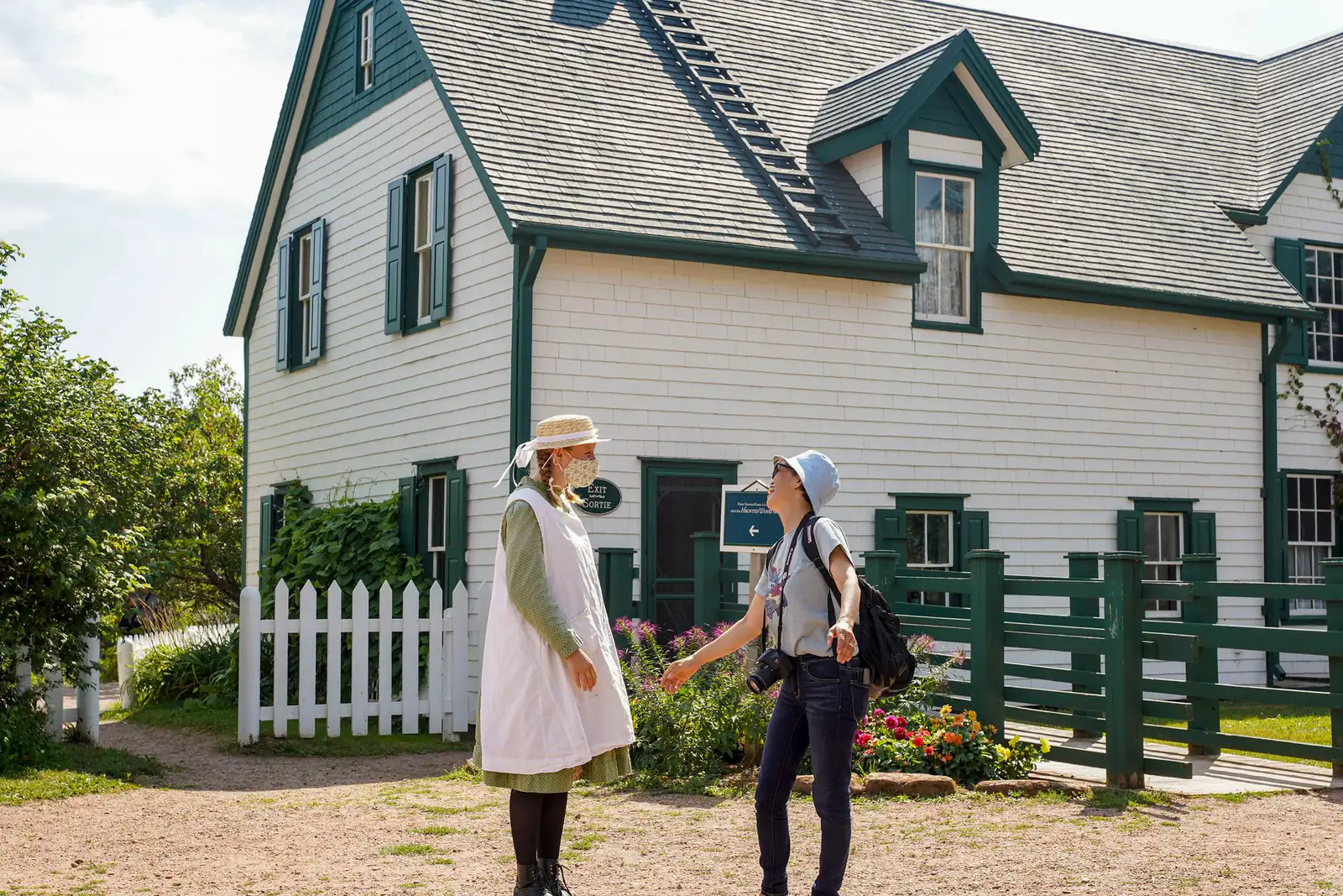 Two women in conversation outside a white heritage house with green trim on Prince Edward Island