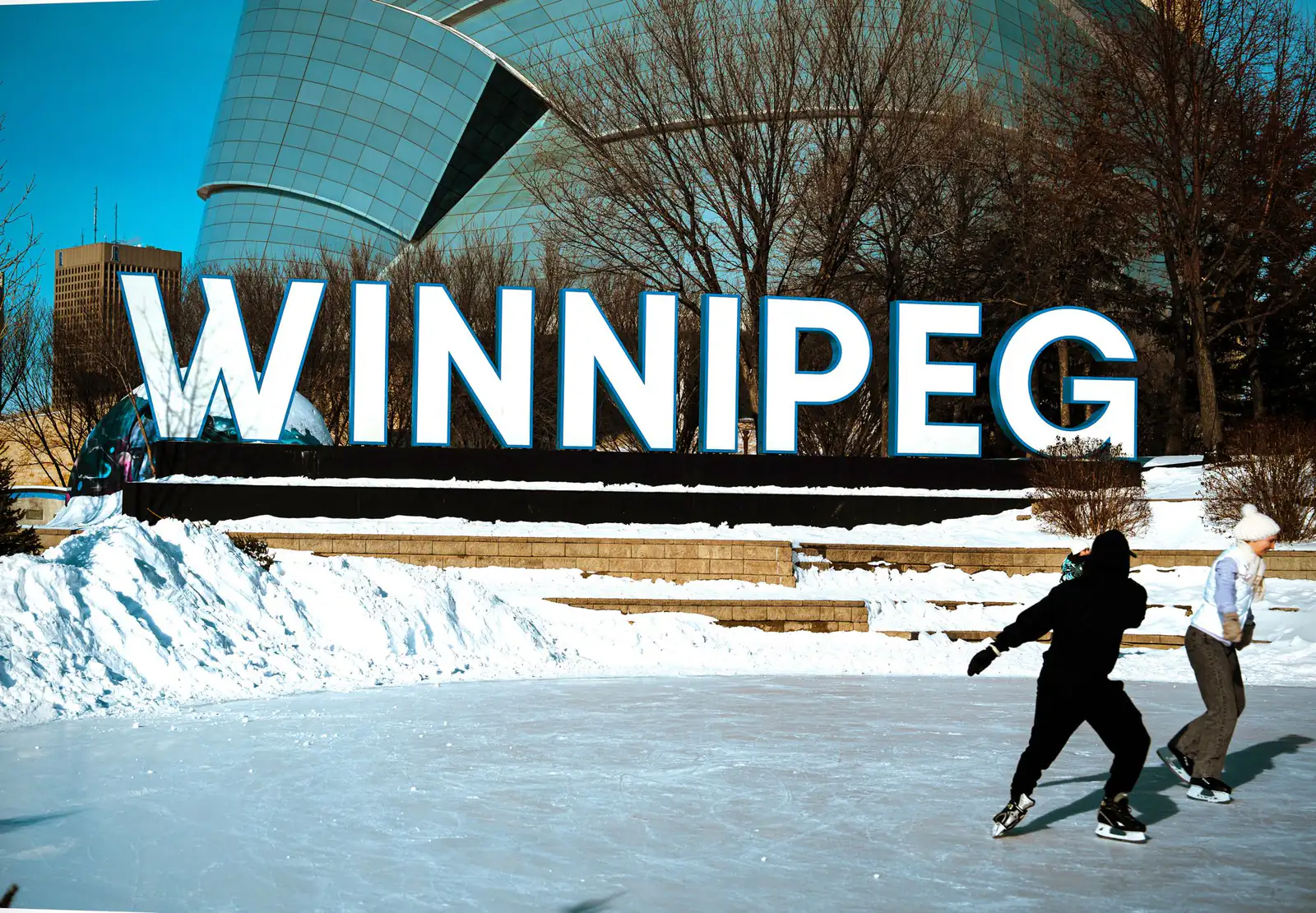 People skating on an outdoor rink beside a large illuminated Winnipeg sign in winter